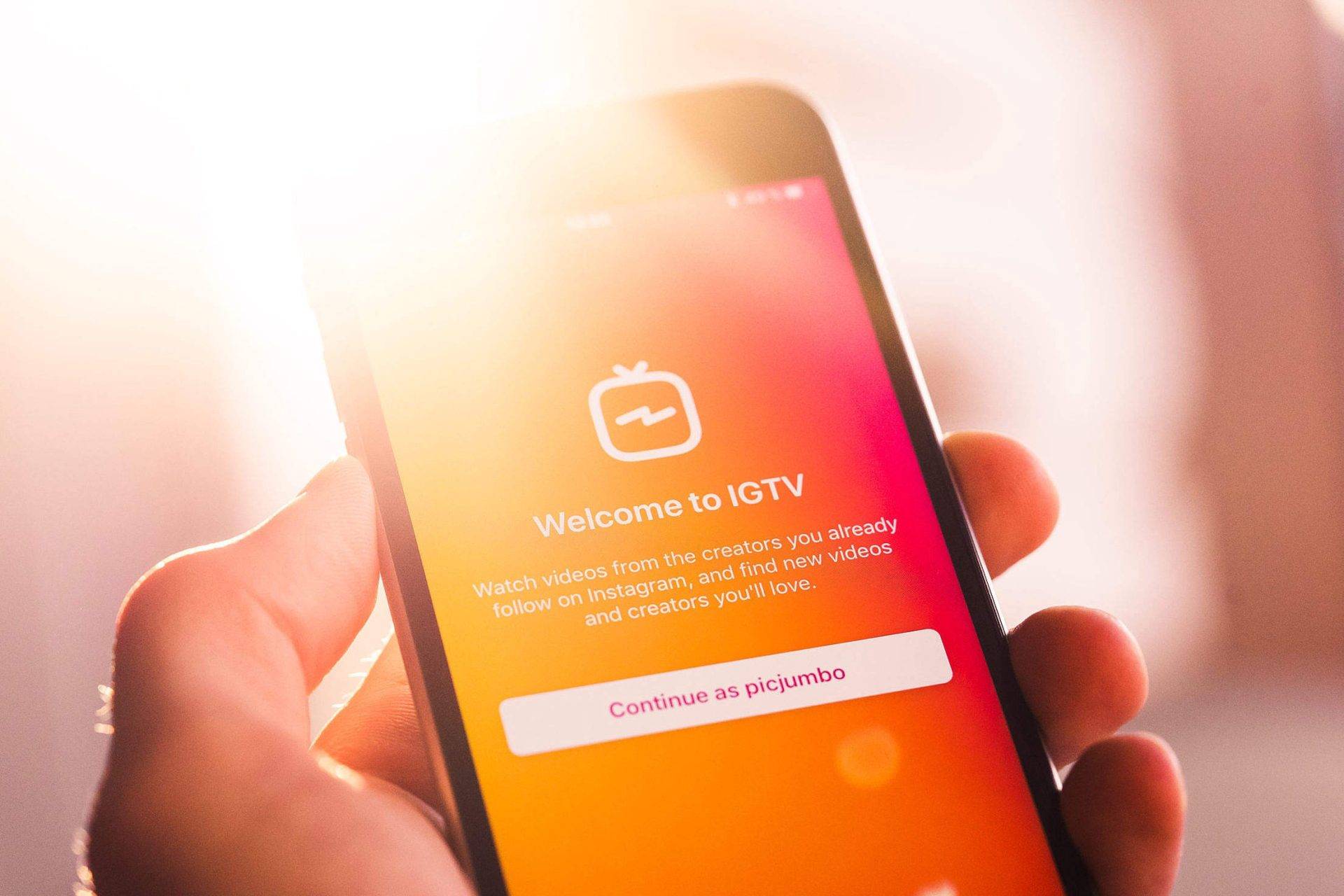  A hand holding a phone with the Instagram app open on the 'Welcome to IGTV' screen, which displays system requirements for the app.